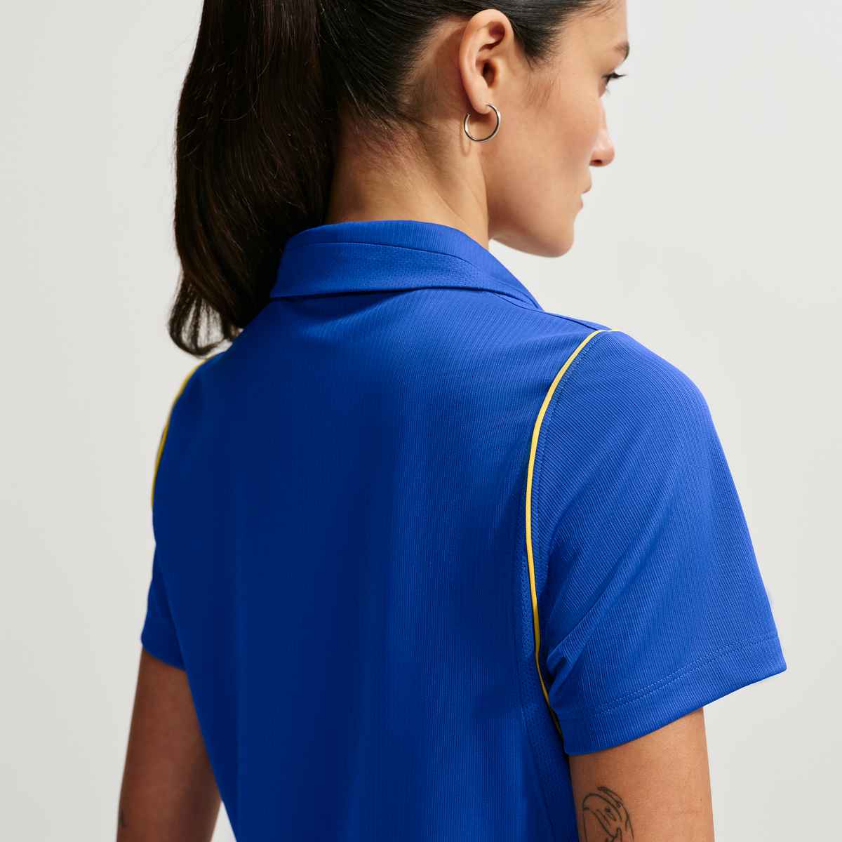 Person wearing a blue polo shirt with yellow accents on a plain background