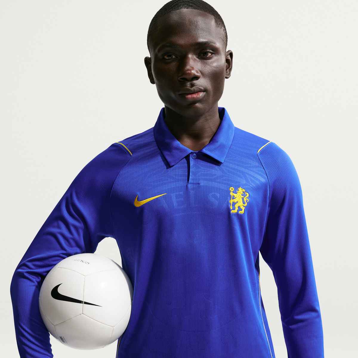 Person wearing a blue sports jersey with a logo, holding a white ball on a light gray background