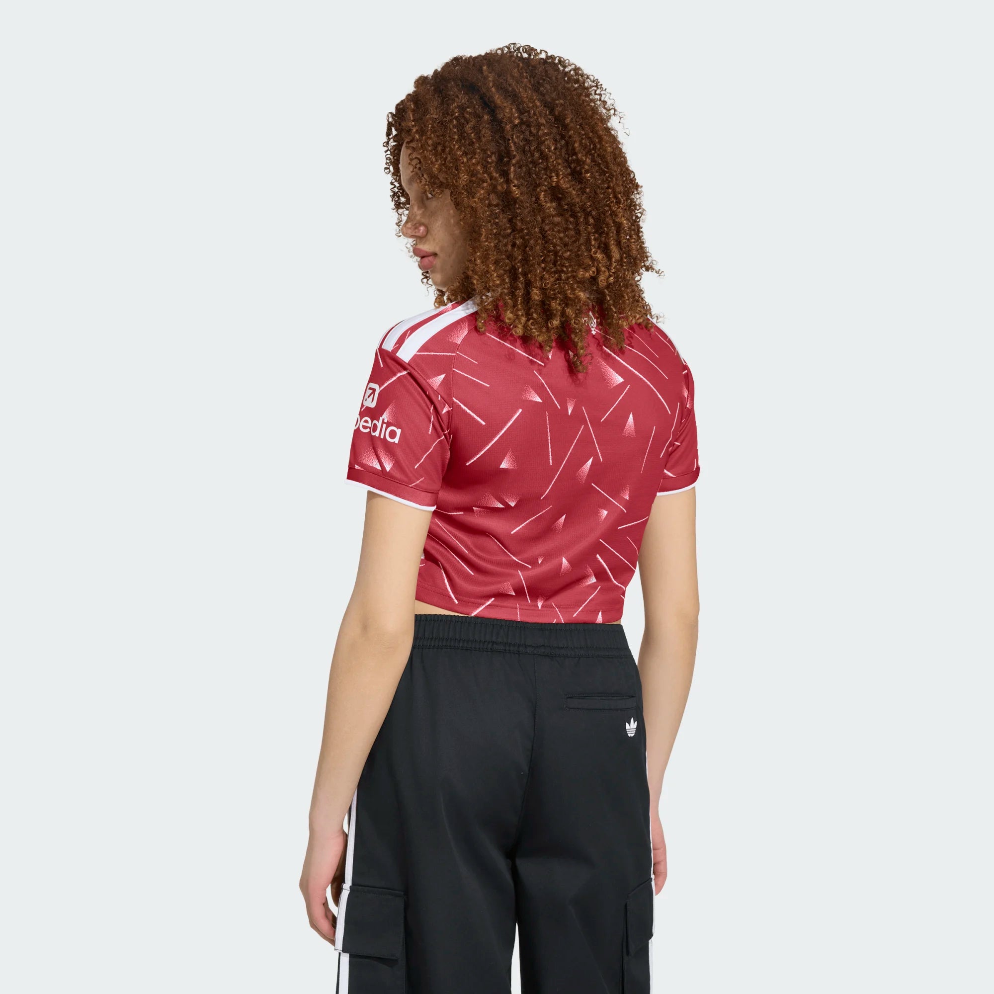 Person wearing a red sports jersey with white patterns and black pants on a white background