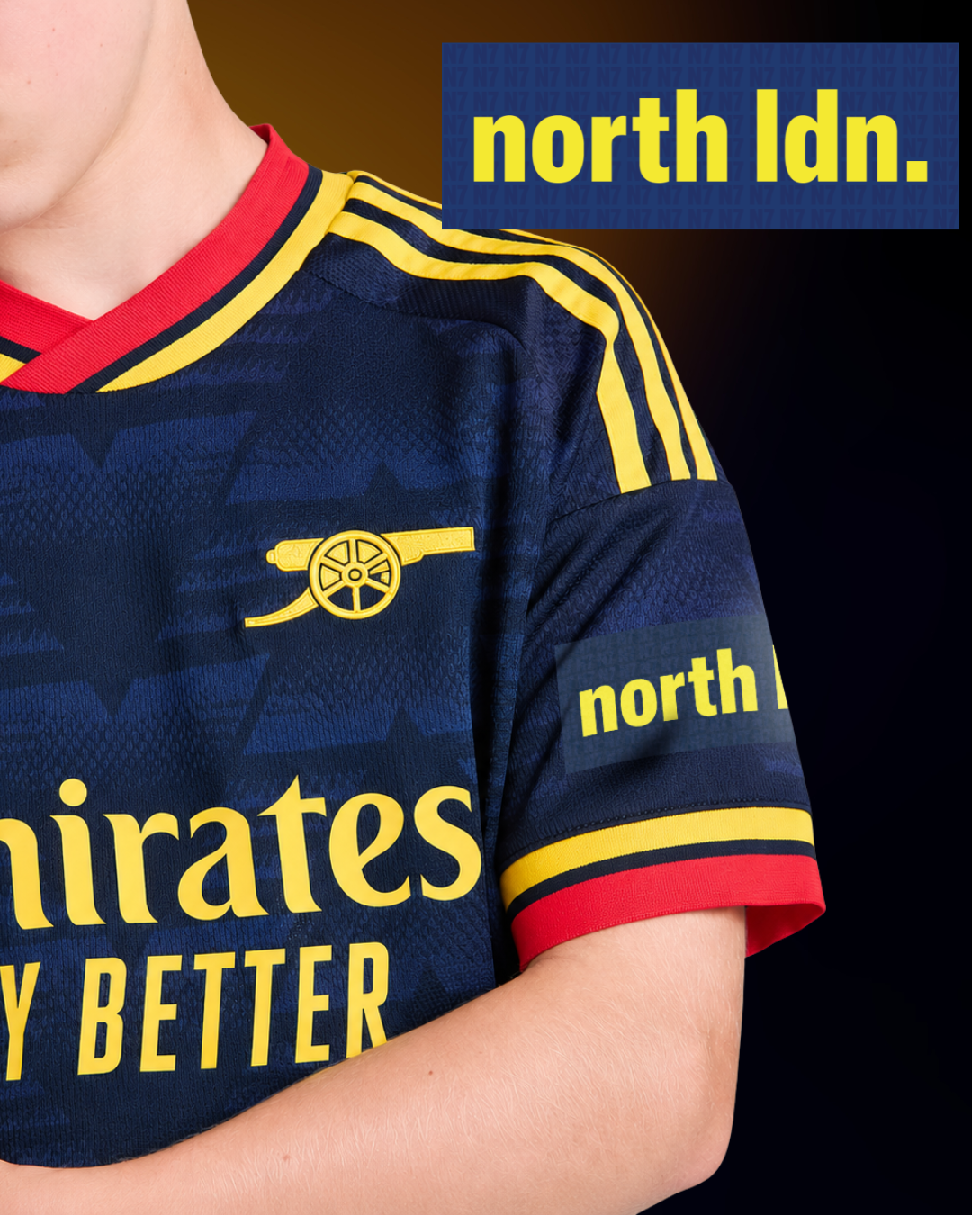 A close-up of a person wearing a dark navy Arsenal football jersey with yellow and red trim, featuring the Arsenal cannon logo and 'north' sponsor text on the sleeve, with a blue 'north ldn.' graphic overlay at the top right.